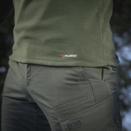 Grøn M-Tac Delta Polartec Fleecejakke viser Polartec-logoet, fremstillet af slidstærkt og åndbart materiale, perfekt til kulde.