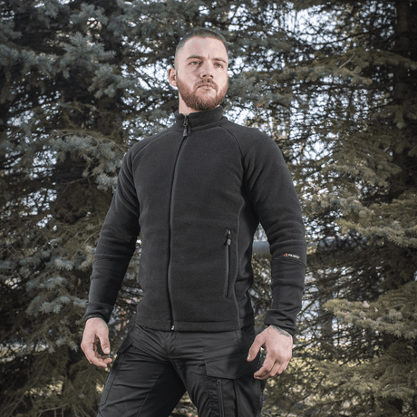 Mand iført M-Tac Polartec Sport Fleecejakke i sort, perfekt til både overgangsperioder og koldt vejr, omringet af træer.