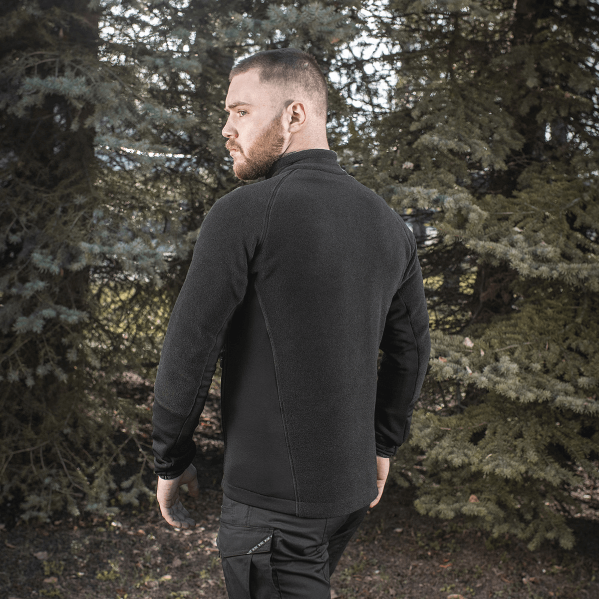 Mand iført M-Tac Polartec Sport Fleecejakke, stående i skoven og demonstrerer fleecejakkens komfort og funktionalitet.