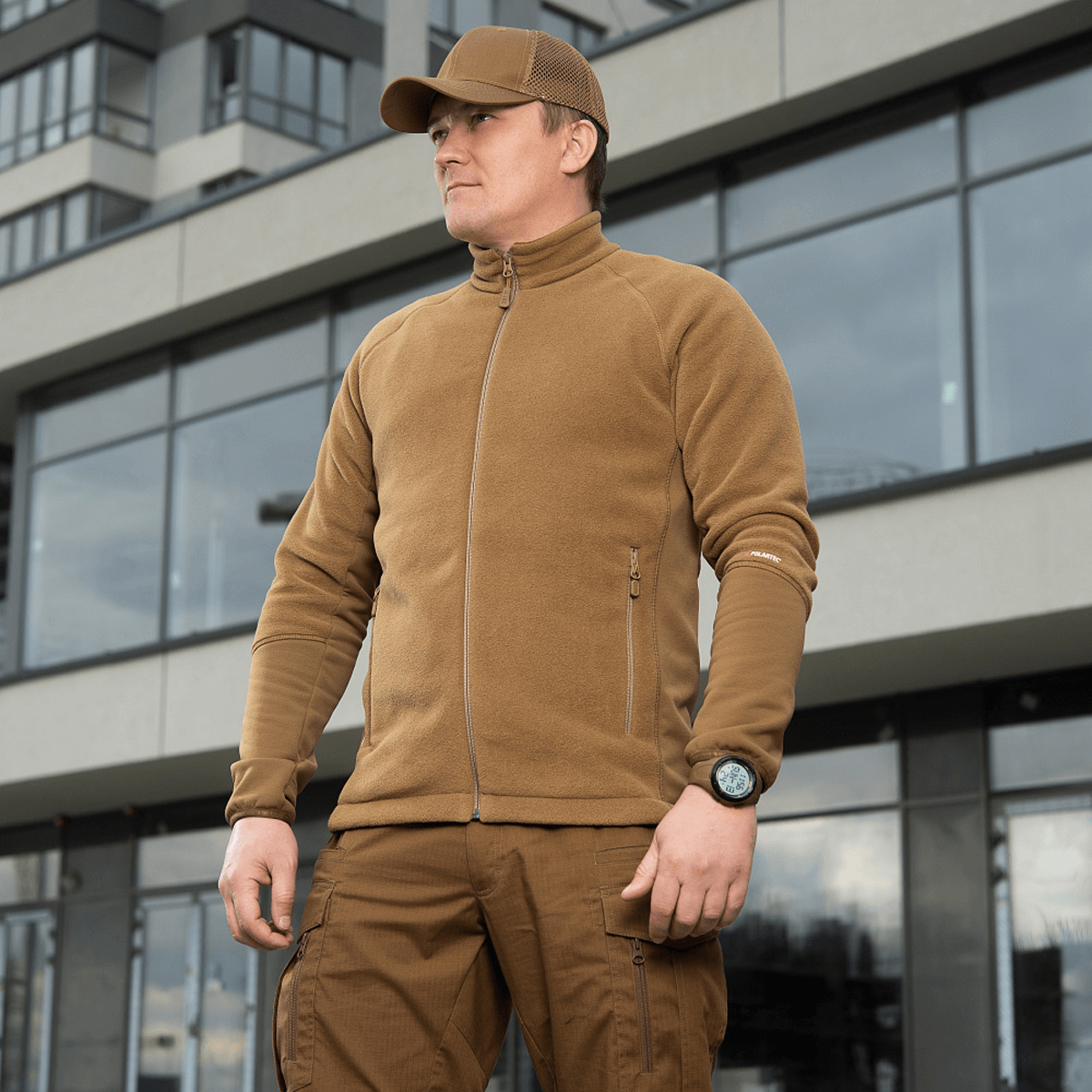 Mand iført M-Tac Polartec Sport Fleecejakke foran moderne bygning, viser fleecejakkens stil og komfort til køligt vejr.