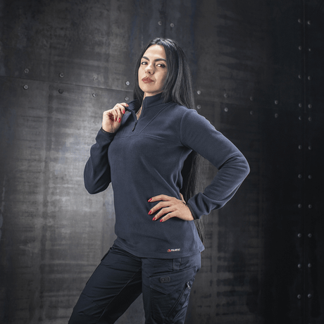 Kvinde iført M-Tac Delta Polartec Fleecejakke Dame, designet til komfort og varme, mod en industrielt stil baggrund.