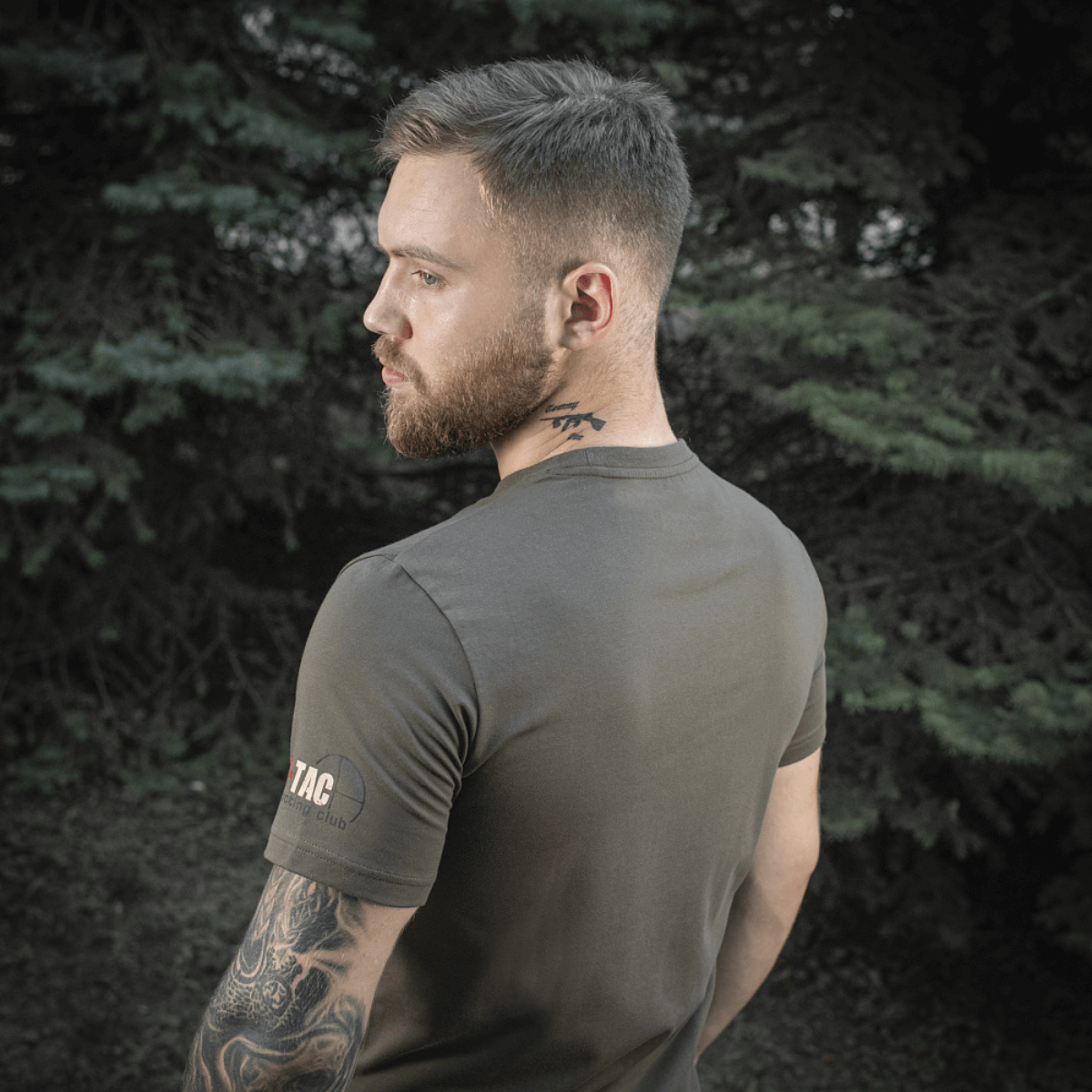 Mand bærer M-Tac Sniper T-shirt i skovmiljø, viser holdbar og komfortabel pasform af 93% bomuld og 7% elastan, ideel til udendørs brug.