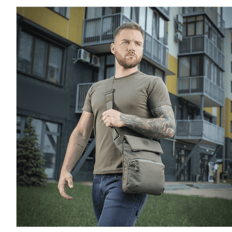 Mann med M-Tac Konvert Taske Elite i grått bymiljø, bærer en moderne veske i nettbrettdesign laget av holdbart Cordura-materiale.
