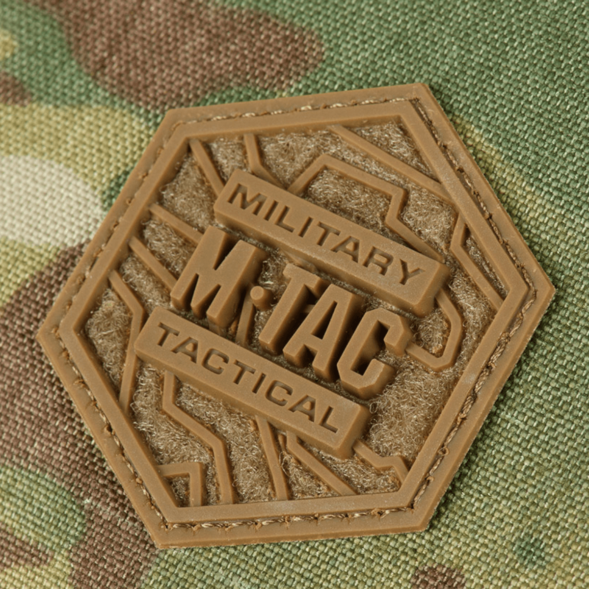 Nærbillede af M-Tac logo på M-Tac Konvert Taske Elite lavet af slidstærk Cordura, camouflagemønster baggrund.