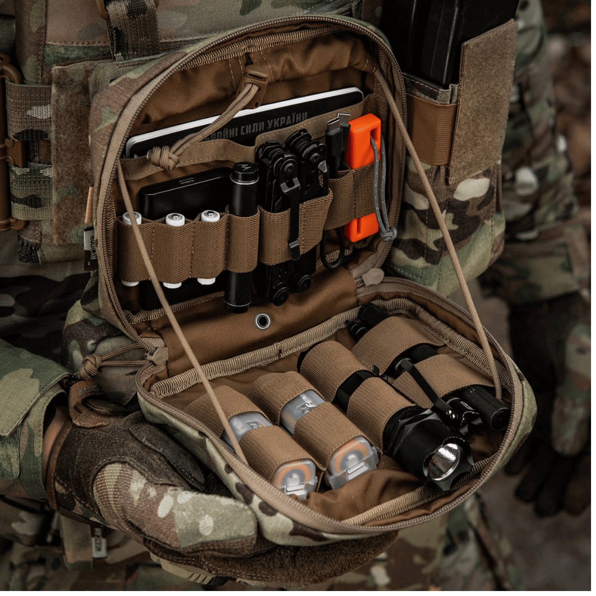 M-Tac organizer pouch Elite til taktiske formål med førstehjælps- og EDC-udstyr i kamouflage baggrund. Ideel til M.O.L.L.E.-systemet.