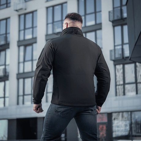 M-Tac Soft Shell Jakke med en vandafvisende membran og fleece-foring, set bagfra mod moderne bygning.