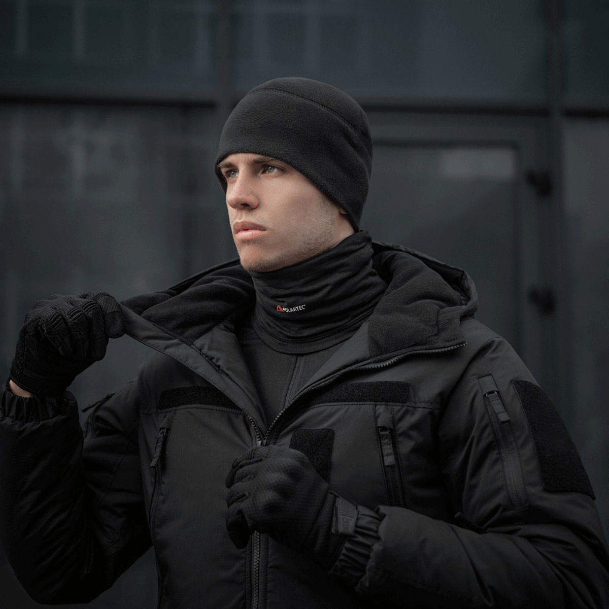 Person iført M-Tac Tube Scarf Polartec Power Grid, sort jakke og hue, til beskyttelse mod kulde og vind.