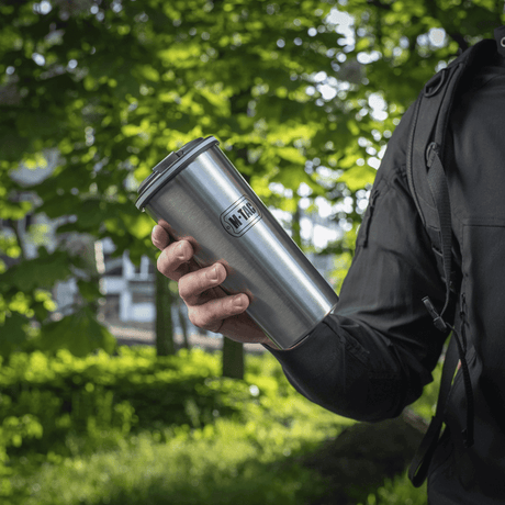 Person holder en M-Tac termokopp 450 ml med ventil i en grønn skog.