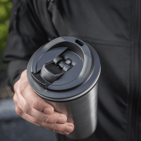 Person holder M-Tac termokopp 450 ml med ventil, designet for å holde drikken varm eller kald, med praktisk tut og rustfritt stål konstruksjon.