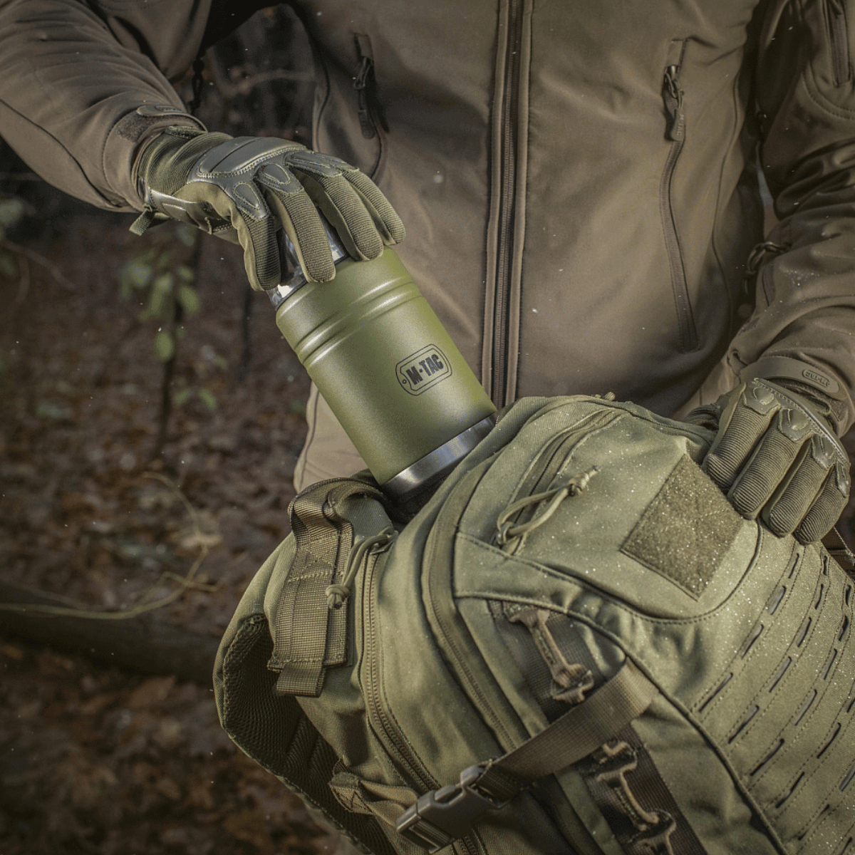 Udendørs brug af M-Tac Termoflaske 750 ml med Folde-ske og rygsæk i skovsætter, der viser flaskens bærbarhed og funktionalitet.