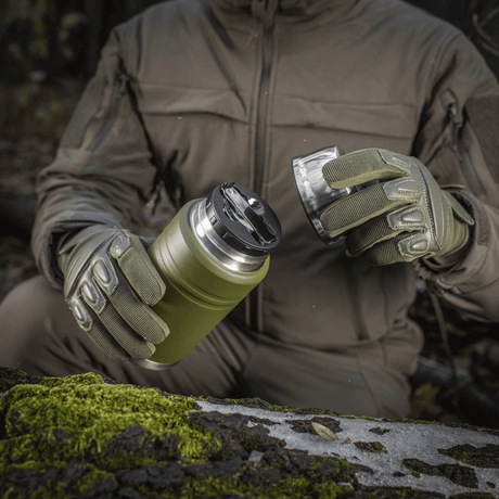 Friluftssituasjon med M-Tac Termoflaske 750 ml med sammenleggbar skje i hanskekledde hender, ideell for camping og utflukter.