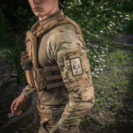 Mann i kamuflasje med M-Tac Patch Ace of Spades på armen i naturmiljø.