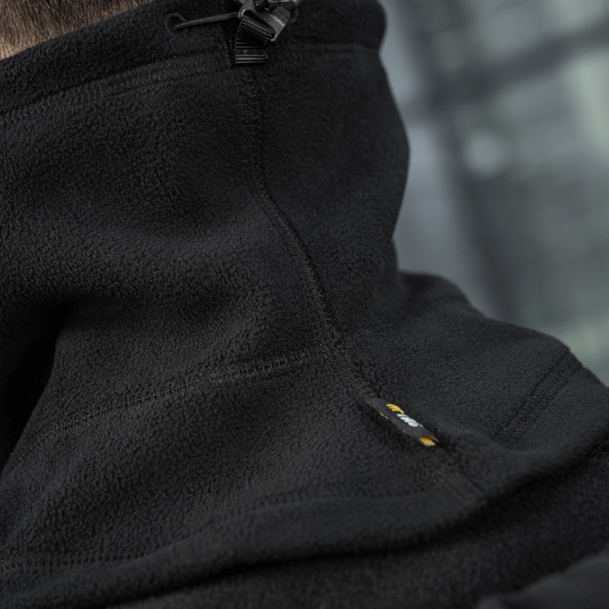 Close-up af M-Tac Anatomisk Snood Justerbar Elite Fleece (320 g/m²) i sort fleece, viser justeringssnøre og slidstærkt materiale.