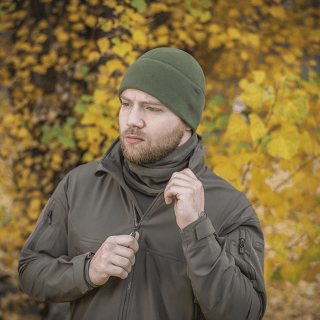 Mand iført grøn M-Tac Fleece Polartec Watch Cap i efterårslandskab, ideal til udendørs aktiviteter i kølige og kolde vejrforhold.