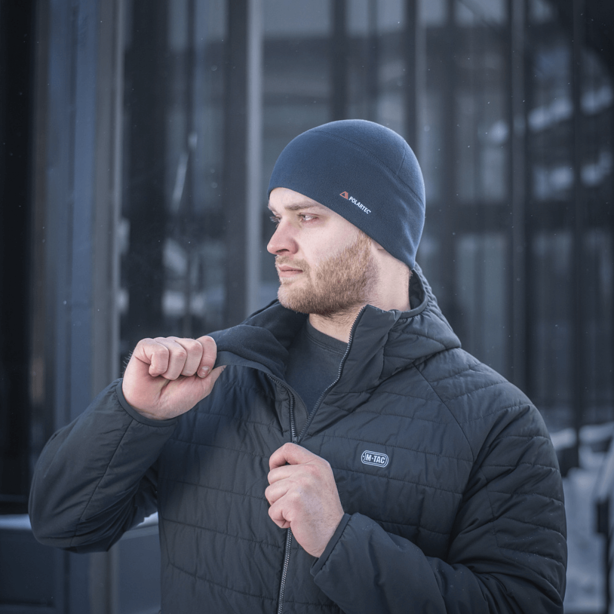 Mand iført M-Tac Fleece Watch Cap Light Polartec vinterhue, stående udendørs i koldt vejr, iført en varm jakke.