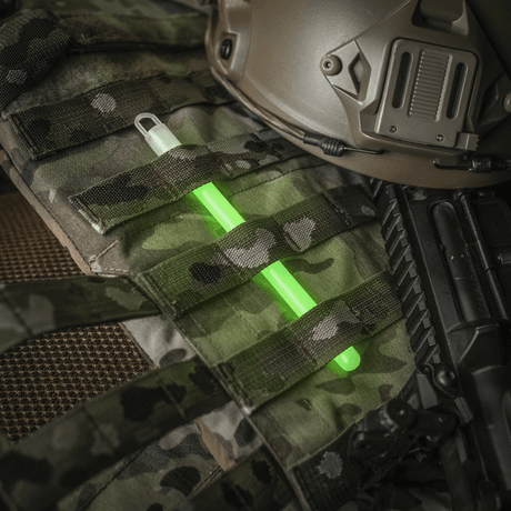 M-Tac Glow Stick 15 cm plassert på militært utstyr, ikke-giftig og allsidig lysstav for sikkerhets- og nødsituasjoner.