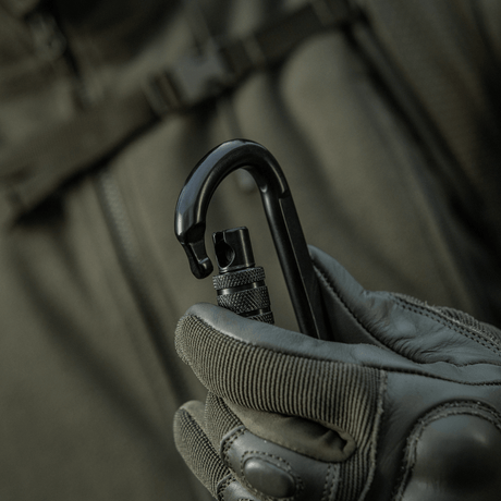 Person holder M-Tac Karabinhage 10 cm i handske, robust trapezformet karabinhage af 40Cr legeret stål til rebslynger.