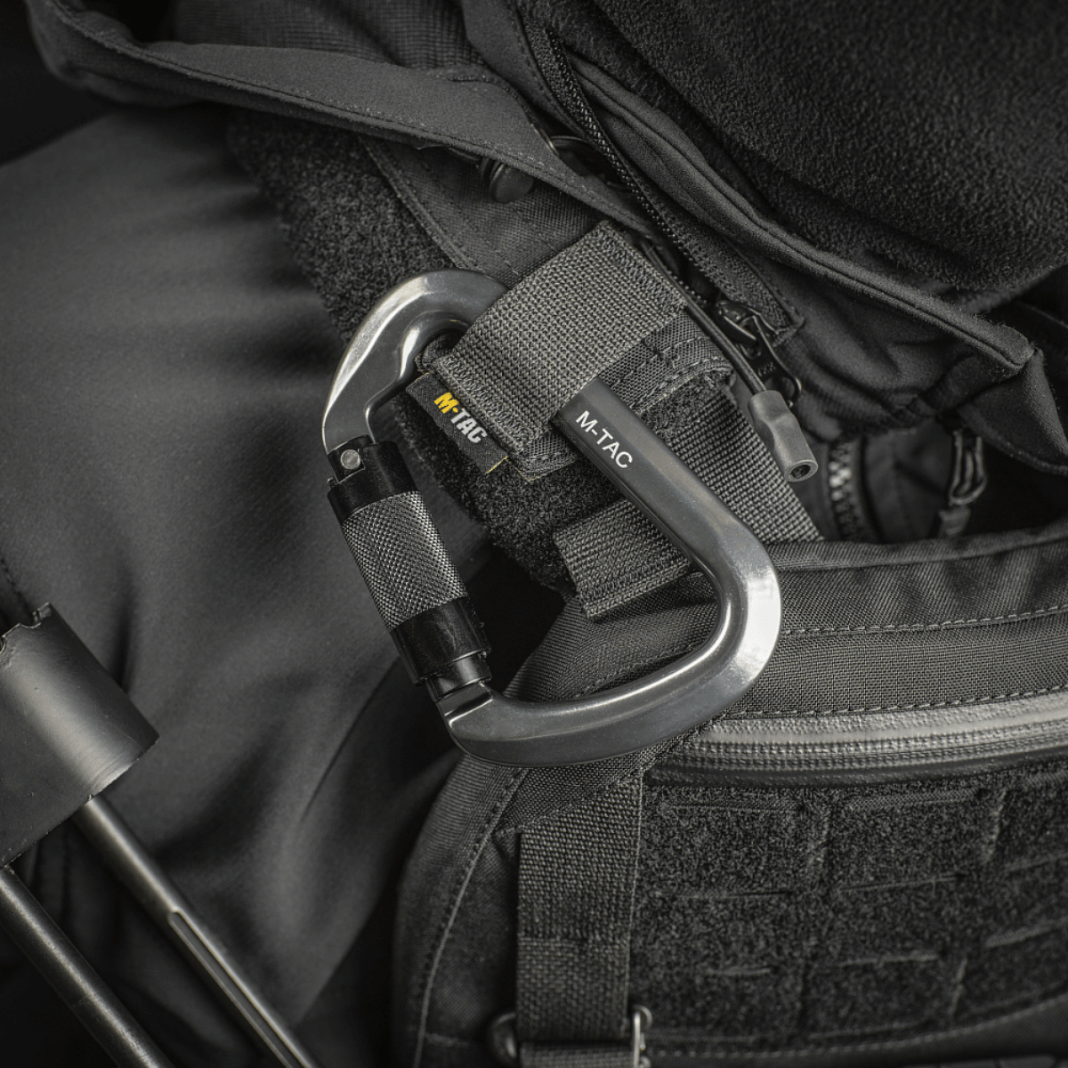 M-Tac Key-Lock Karabinhage af aluminium, monteret på sort udstyr, ideel til klatring og sikkerhed. Ergonomisk designet, CE EN362 standard.