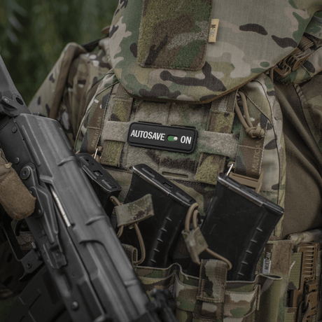M-Tac Patch Autosave PVC på en kamuflasjejakke med magasinlommer, viser detaljert 3D-design og fargeklarhet, egnet for taktisk bruk.