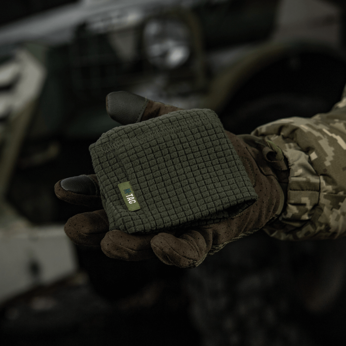 M-Tac Rip-Stop Fleece Hjelmliner vises i en hånd iført taktik handsker i et udendørs militært miljø, kompakt og klar til brug.