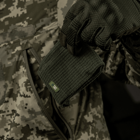 M-Tac Rip-Stop Fleece Hjelmliner - varm og slidstærk fleece hjelmliner i hånden, perfekt til køligt vejr, set mod camouflagebaggrund.