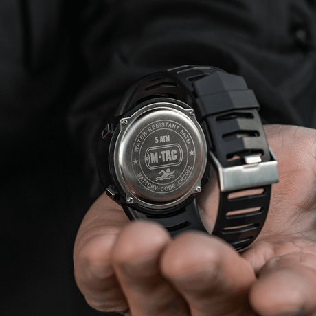 M-Tac Tactical Ur 2147 med stållokk, "WATER RESISTANT 5ATM" og "BATTERY CODE CR2032" vises i en hånd.