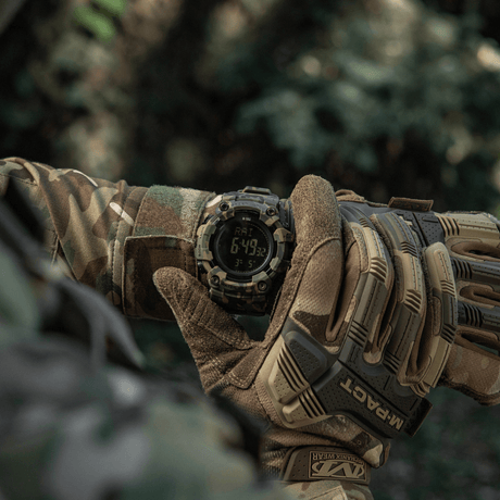 M-Tac Tactical Ur 2037 i bruk i naturen, vist på håndleddet til en person i camotøy, viser LED-bakgrunnsbelyst skjerm og funksjoner.