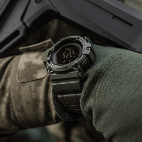 M-Tac Tactical Ur med Kompass 2233 på militærkledd arm, for utforskning og utendørs eventyr, robust ur designet for taktisk bruk med kompass og LED-skjerm.