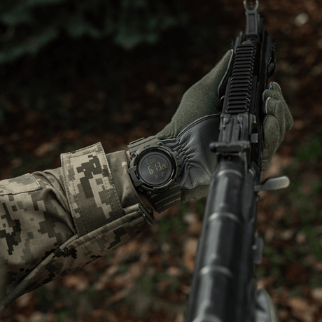 M-Tac Tactical Ur med Kompass 2233 båret av person i kamuflasje med rifle, viser holdbarhet og funksjonalitet i villmarken.