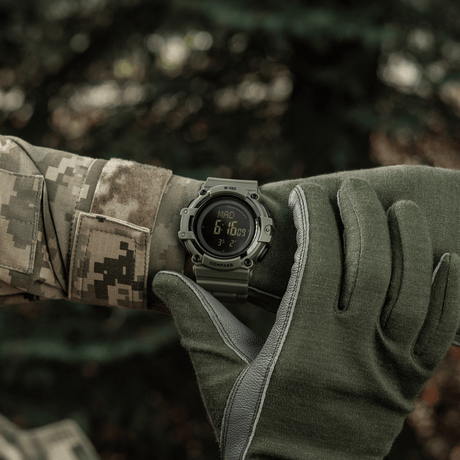M-Tac Tactical Ur med Kompass 2233 båret av soldat utendørs, viser robust design og funksjoner som LED-belysning og 5ATM vannmotstand.