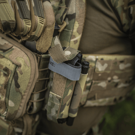 M‑Tac Tourniquet Pouch Elastic Gen.5 festet til taktisk utstyr i camo-design, med en tourniquet sikkert oppbevart.