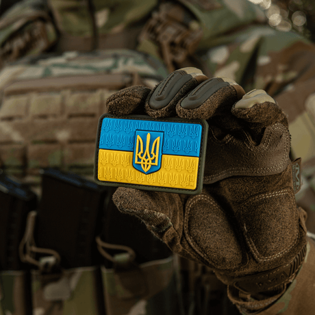 M-Tac Patch Ukraine-flagg med våpenskjold i PVC med 3D Trident, holdes av en person i militært kamuflasjetøy.