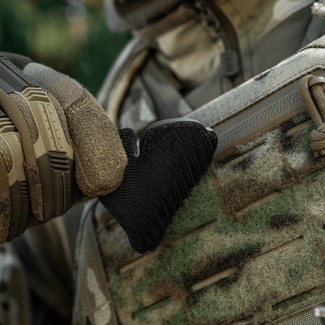 Taktisk hanske justerer svart velcro-patch på kamuflasjedrakt utendørs.