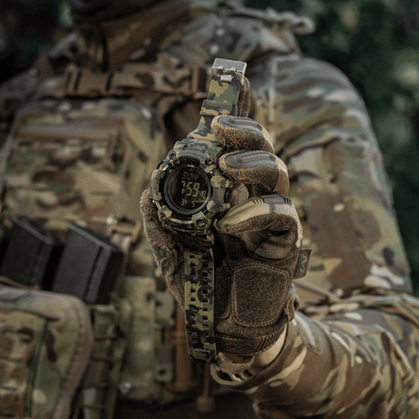 M-Tac Tactical Ur 2037 i kamuflasje, båret av person i taktisk bekledning, viser klokke og dato, ideelt for utendørs og daglig bruk.