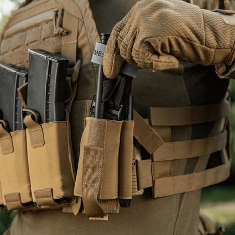 Person iført taktisk vest med M‑Tac Tourniquet Pouch Elastic Gen.5, Coyote Brown, for sikker oppbevaring av CAT tourniquet.