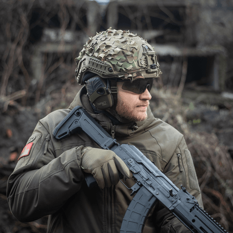 Soldat iført M‑Tac Vilha Hjelmcover FAST i Camouflage med rifle, klar for terrengutfordringer. Slitesterkt materiale, optimal passform.