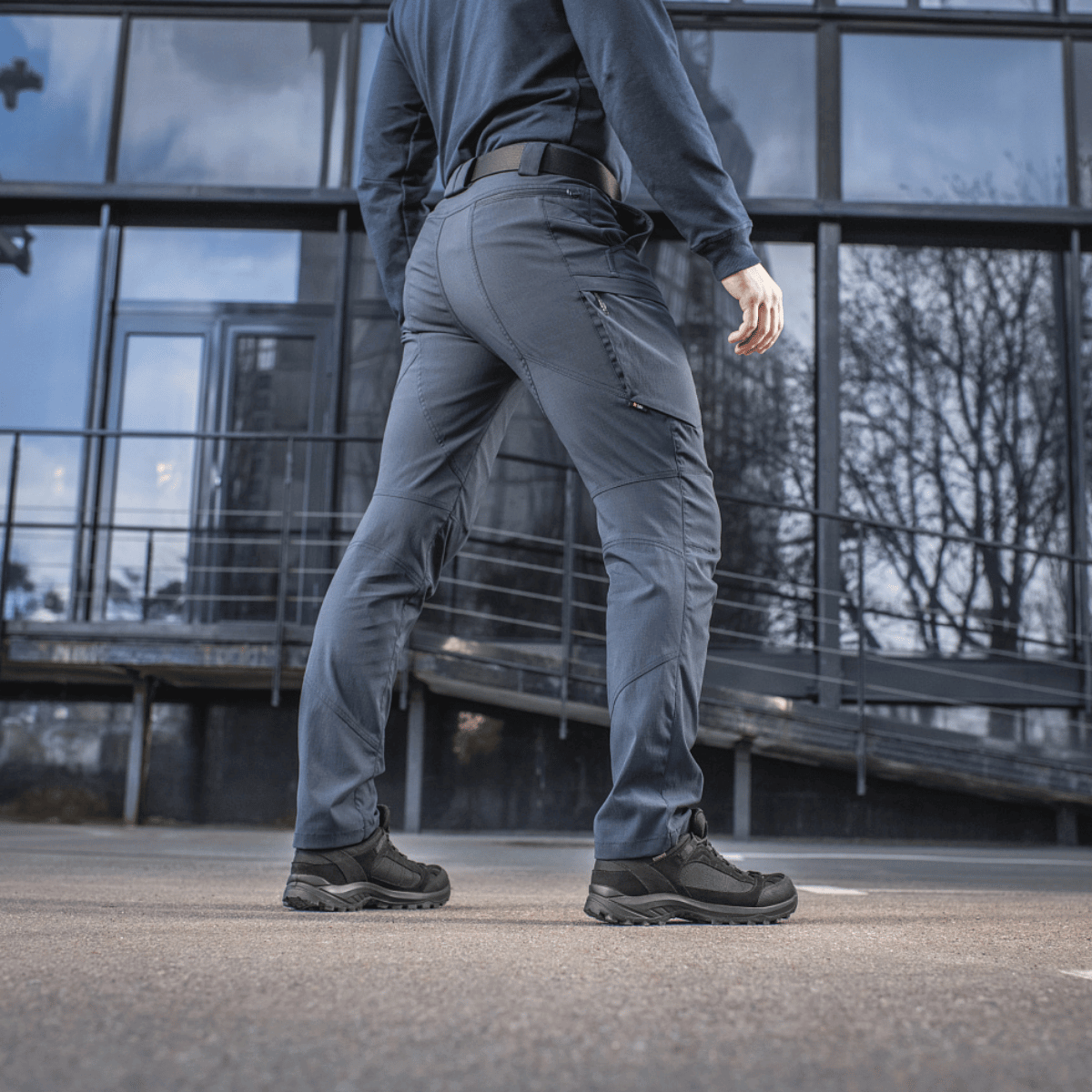 Person i M-Tac Bukser Sahara Flex Light foran moderne bygning, der fremhæver komfort og stilfuldt design.