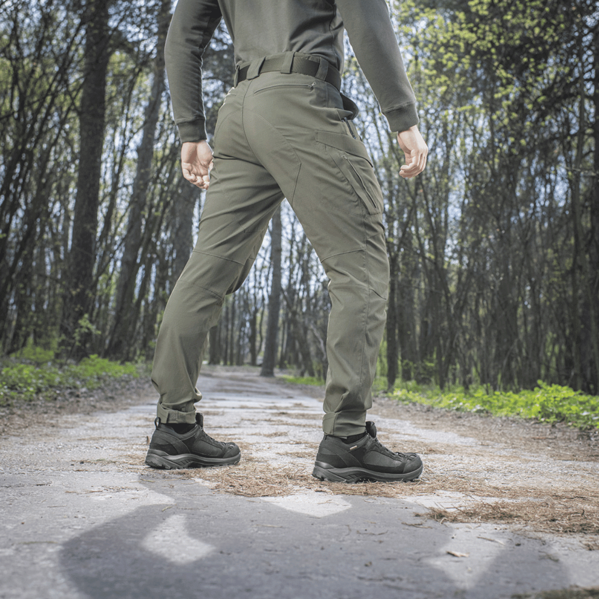 Mand bærer M-Tac Bukser Aggressor Summer Flex i skovmiljø, ideelle til varmt vejr med let Rip-Stop nylonstof.
