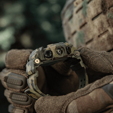 M-Tac Tactical Ur 2037 holdt av person med hansker, utendørs miljø, robust design egnet for utendørs, taktisk og daglig bruk.