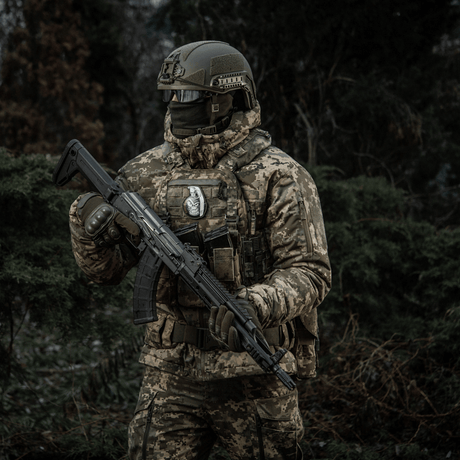 Soldat i kamuflasje med rifle i skog, bærer M-Tac Patch M67 Granat 3D PVC på taktisk vest