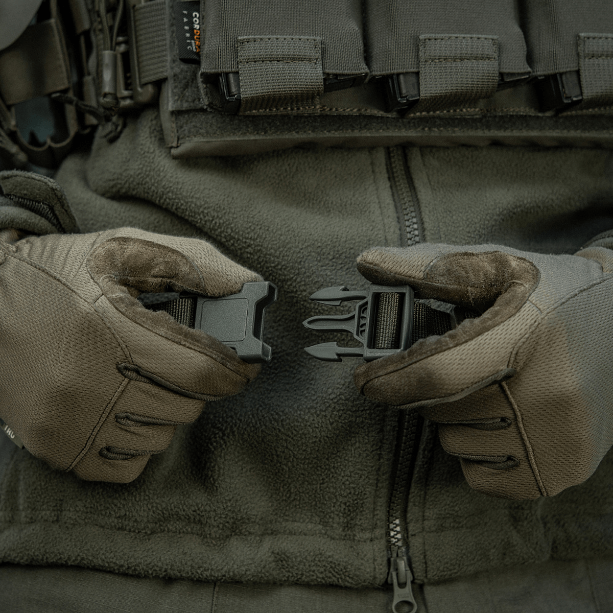 Præsentation af M-Tac Siddeunderlag med bælte brugt i taktisk miljø med handsker, klar til kold vejr udendørs aktiviteter.