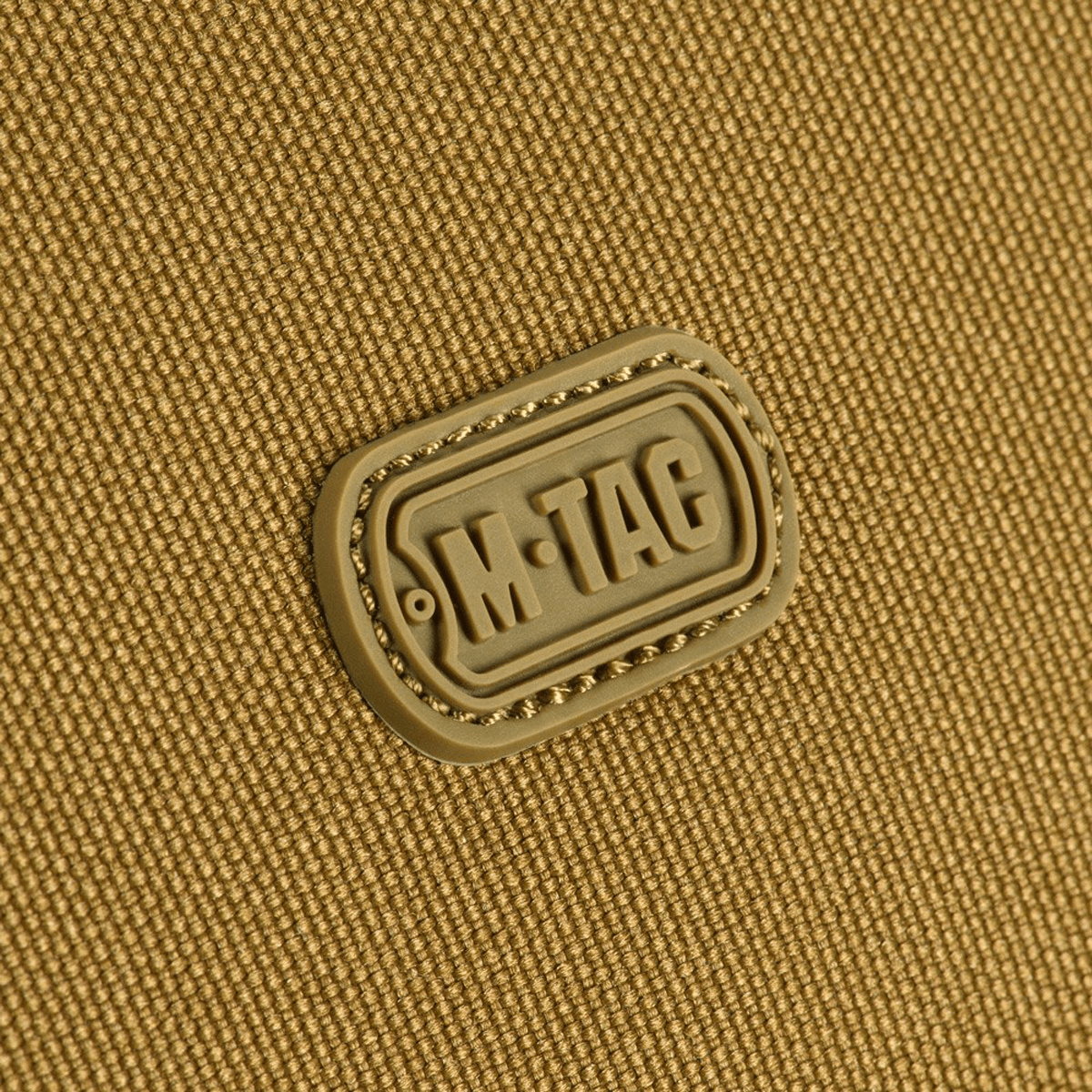 Close-up af M-Tac Toilettaske logo på slidstærkt 600D polyester med PVC-belægning, perfekt til kompakt opbevaring og rejsebrug.