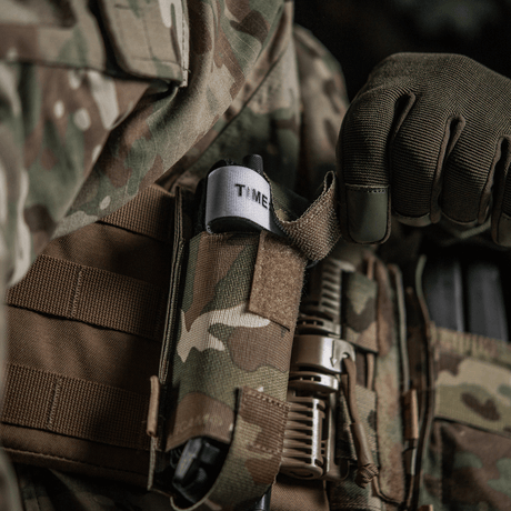 M-Tac Elastisk Tourniquet Pouch Molle Gen.III i kamuflage, fastgjort til taktisk vest med tourniquet synlig.