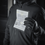 Person holding pasbeskyttelse M-Tac Pascover til ukrainske pas, visende "Passport" tryk, polymerkomposit, sort baggrund.