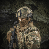 Person wearing M‑Tac Hjelmcover Shroud Elite in MULTICAM, holding rifle, displaying tactical gear outdoors.