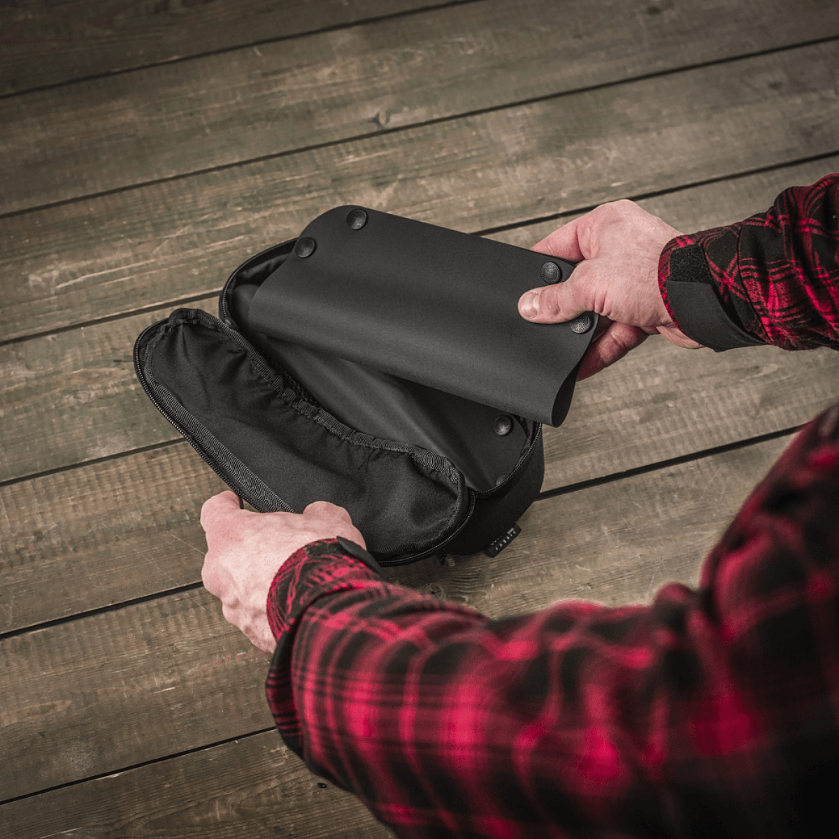 M‑Tac Field Vedligeholdelsesbakke 18x30 cm foldet ud af mand i rød skovmandsskjorte, viser sort moderne polymerkompositmateriale.