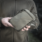 Mand holder en M‑Tac Pocket Bag Elite HEX, en kompakt og robust taske lavet af slidstærkt materiale med YKK lynlåse.