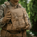 M-Tac Sukharka Gen.3 Pouch i Cordura 500D med MOLLE-interface holdt af en person i camouflagetøj i skovmiljø