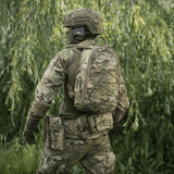 Soldat i camouflageuniform med rygsæk, set bagfra i en skov.