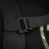 Nærbillede af sort stropspænde på rygsæk med camouflage-trykdetalje, robust konstruktion og sikker lukning.